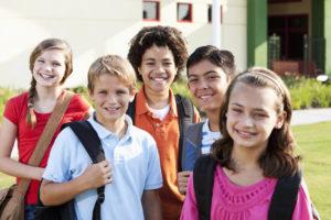 Multi-ethnic elementary or middle school students standing outside school building (10-12 years). Focus on boys in middle row.